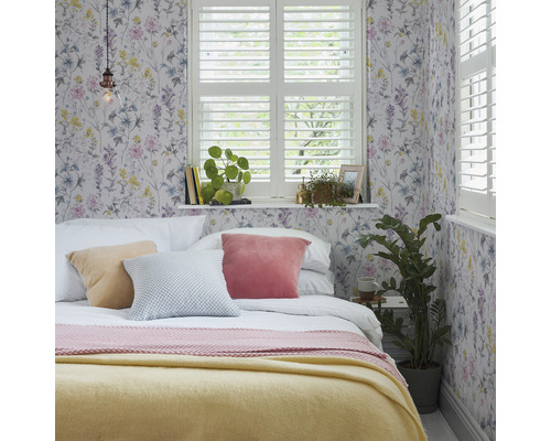 Chambre avec papier peint floral, lit, coussins et fenêtre avec volets