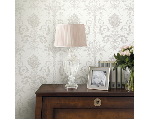 Intérieur décoratif avec papier peint à motifs, lampe, cadre photo, livres et fleurs sur une armoire.