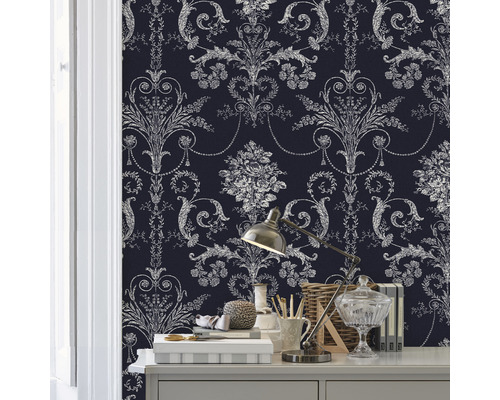 Gros plan d''une pièce avec un mur recouvert d''un papier peint à motifs. Divers objets décoratifs et une lampe sont posés sur une table.