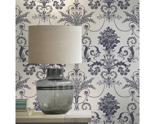 Dekoratives Zimmer mit einer Tischlampe vor einer floral gemusterten Tapete.