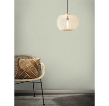 Raumansicht mit Rattansessel, Dekokissen und Rattanlampe vor einer strukturierten Wandtapete.