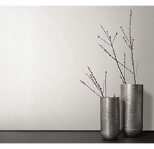 Zwei Metallvasen mit Blütenzweigen vor einer Wand