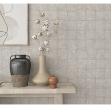 Gros plan sur différents vases et éléments décoratifs sur une table en bois devant un mur à motifs.