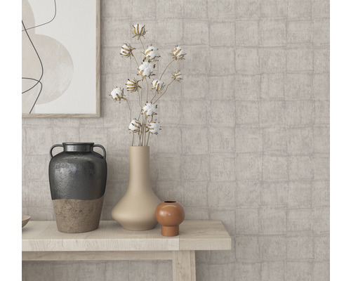 Gros plan sur différents vases et éléments décoratifs sur une table en bois devant un mur à motifs.