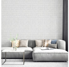 Salon avec canapé gris, table basse et papier peint blanc aspect maçonnerie