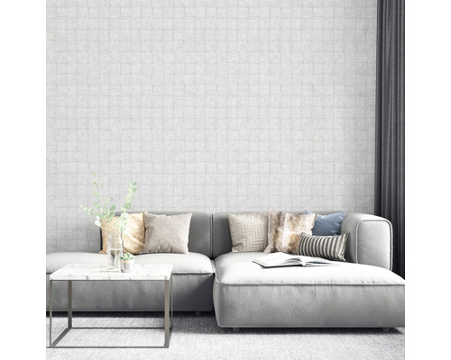 Salon avec canapé gris, table basse et papier peint blanc aspect maçonnerie