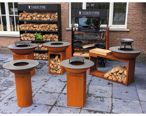 Scène d''extérieur avec divers braseros Tiger Fire, des étagères de rangement pour le bois et des accessoires de barbecue sur une terrasse