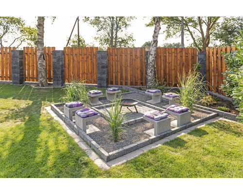 Gartenszene mit Feuerstelle, Sitzgelegenheiten mit Kissen und Holzzaun
