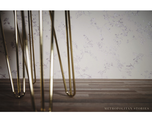 Detailaufnahme von Tischbeinen aus Metall vor einer Wandtapete mit floralem Muster.