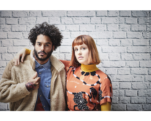 Portrait de deux personnes devant un mur de briques