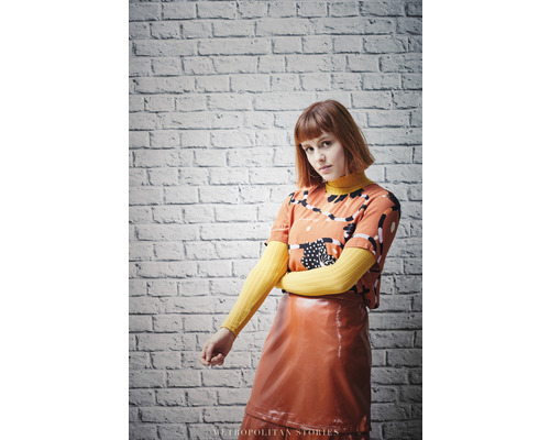 Femme portant un t-shirt à motifs et une jupe brillante devant un mur de briques