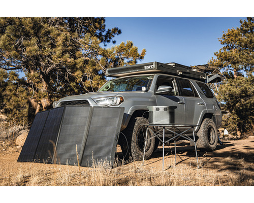 Geländewagen mit Solarmodul und Campingtisch in der Natur