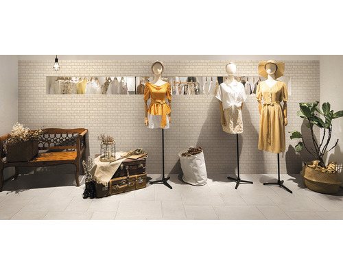 Boutique de mode avec des vêtements sur des mannequins, un banc et des murs carrelés.