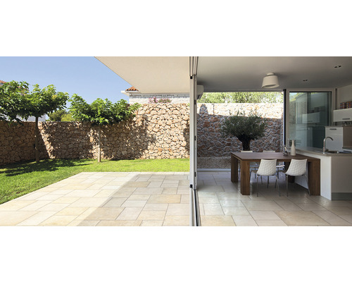 Helle Terrasse mit Natursteinmauer und Übergang zu einem Essbereich im Innenraum