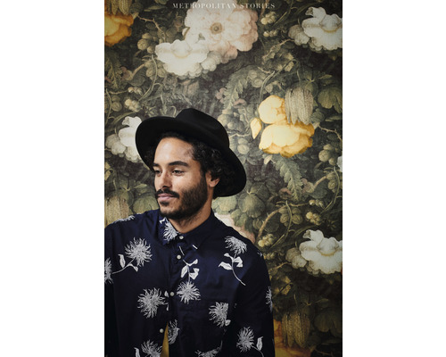 Un homme avec un chapeau devant un papier peint floral de la collection Metropolitan Stories.