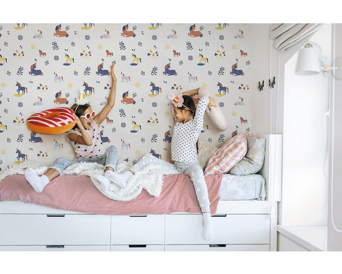 Deux filles sont assises sur un lit devant un mur à motif de licorne.