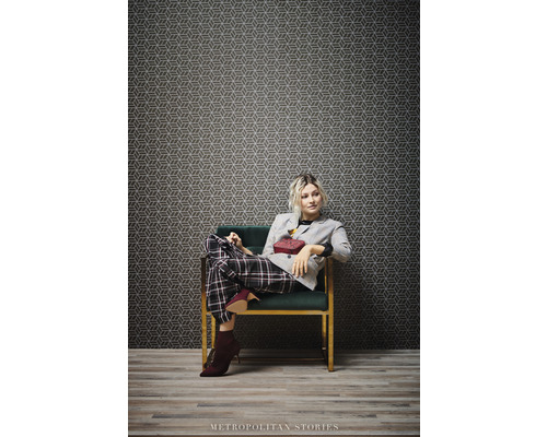Femme assise dans un fauteuil devant un papier peint à motifs géométriques