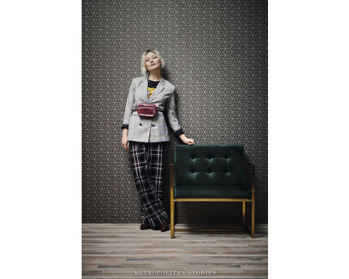 Femme en veste et pantalon à côté d''un fauteuil et de papier peint géométrique