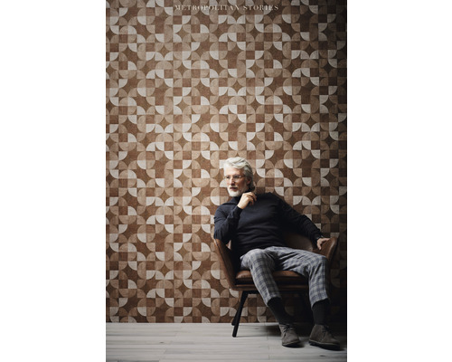 Mann sitzt vor einer Wand mit geometrischer Tapete der Metropolitan Stories Kollektion.
