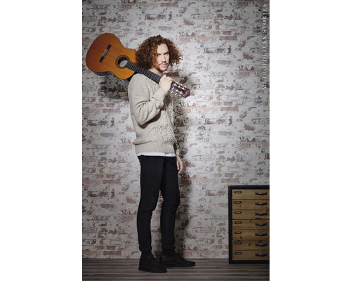 Homme avec une guitare devant un mur de briques
