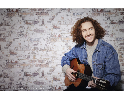 Homme avec une guitare devant un mur de briques
