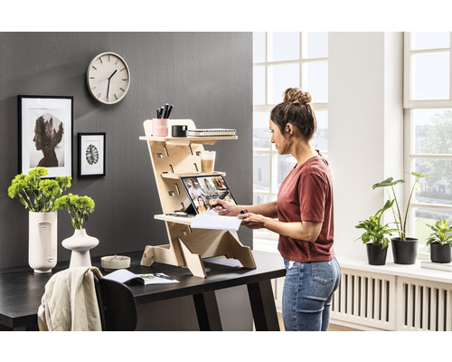 Une femme utilise un bureau surélevé réglable en hauteur en bois sur un bureau dans une pièce lumineuse.