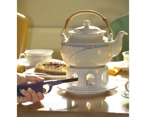 Théière sur une table avec un gâteau et une personne allumant une bougie chauffe-plat