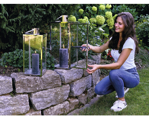 Femme allume une bougie dans un photophore sur un mur de pierre dans le jardin