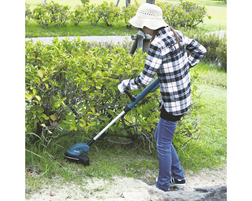Une femme coupe l''herbe avec un coupe-bordures à batterie dans le jardin.