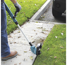 Une personne utilise un coupe-bordure pour tailler l''herbe le long d''un trottoir.