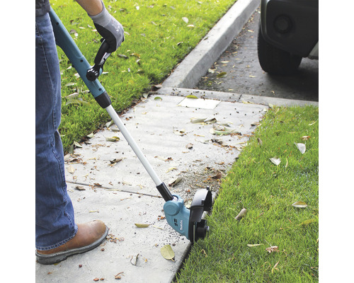 Une personne utilise un coupe-bordure pour tailler l''herbe le long d''un trottoir.