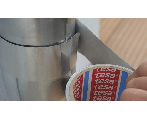 Eine Person befestigt ein silbernes Metallrohr mit Tesa-Klebeband.