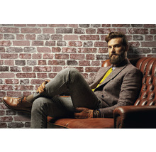 Mann sitzt auf Ledersofa vor einer Ziegelwand