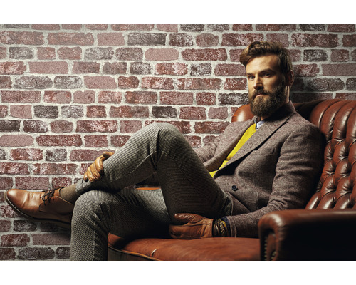 Mann sitzt auf Ledersofa vor einer Ziegelwand