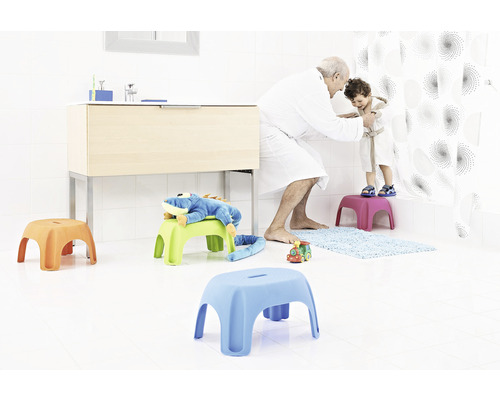 Salle de bains avec meuble-lavabo, rideau de douche et plusieurs tabourets pour enfants sur lesquels se tiennent un enfant et un adulte
