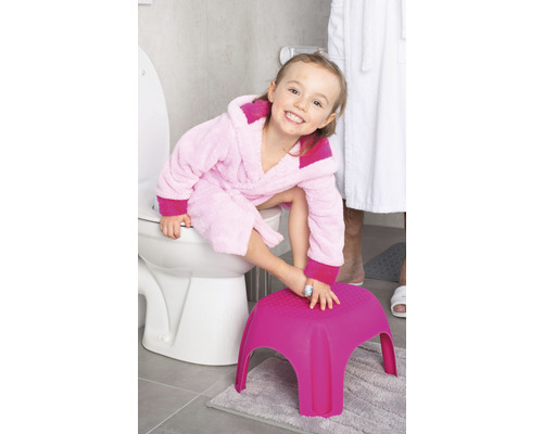 Fille en peignoir sur un siège de toilette avec un tabouret dans la salle de bain