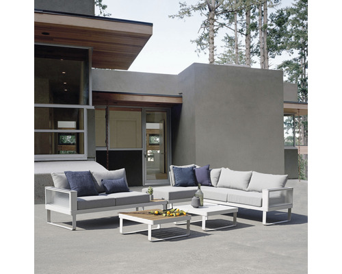 Eine moderne Gartensitzgruppe mit Sofa, Sessel und Tischen auf einer Terrasse vor einem modernen Haus.