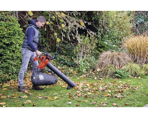 Un homme utilise un aspirateur de feuilles dans le jardin pour enlever les feuilles.