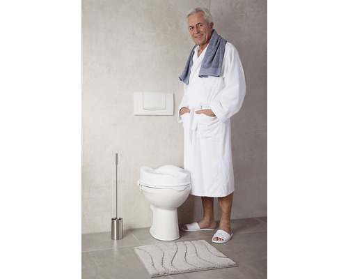 Badezimmer mit erhöhtem WC-Sitz, Toilettenbürste, Badematte und einer Person im Bademantel