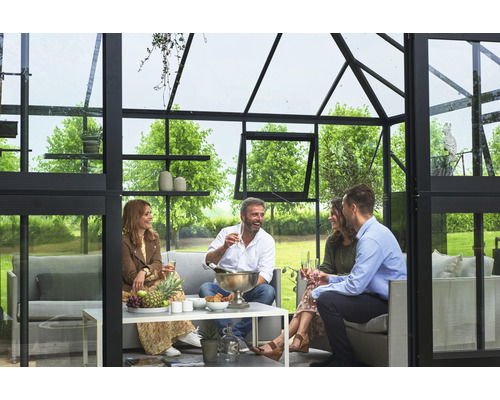 Gruppe von Personen geniesst eine gesellige Runde in einem Gewächshaus mit Sitzgelegenheiten und Tisch.