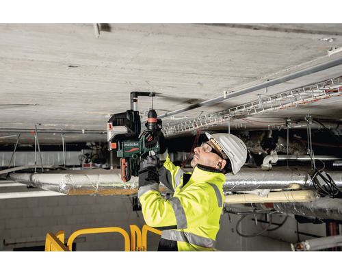 Un homme perce un trou dans un plafond en béton avec une perceuse Metabo.