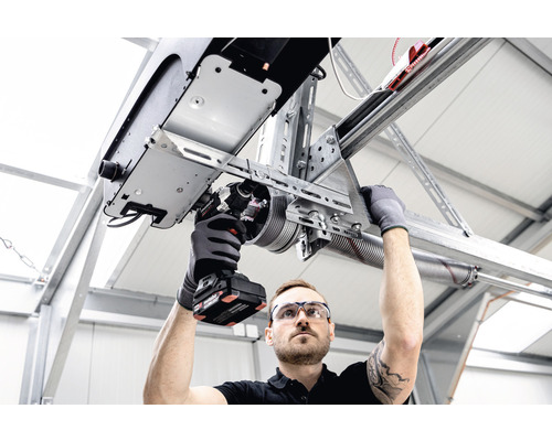 Un homme installe un ouvre-porte de garage avec une visseuse sans fil.