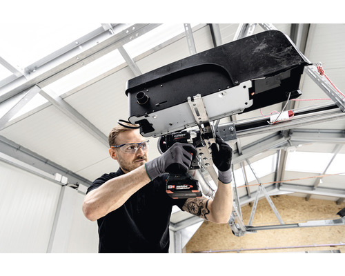 Un homme installe un ouvre-porte de garage avec un tournevis sans fil.