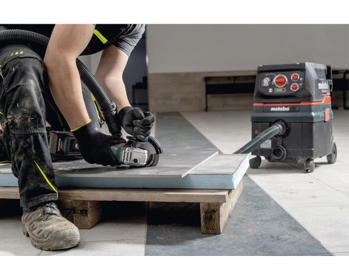 Handwerker schneidet Fliese mit einem Winkelschleifer, angeschlossen an einen Industriestaubsauger der Marke Metabo