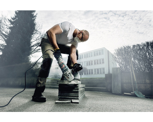 Un homme coupe des pierres avec une meuleuse d''angle à l''extérieur.