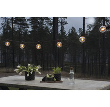 Scène avec une guirlande lumineuse au-dessus d''une table avec des fleurs et des boissons à l''extérieur.