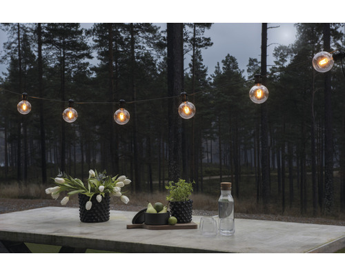 Scène avec une guirlande lumineuse au-dessus d''une table avec des fleurs et des boissons à l''extérieur.