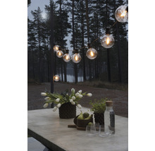 Table décorée avec des fleurs, des fruits et des verres sous une guirlande lumineuse à l''extérieur.