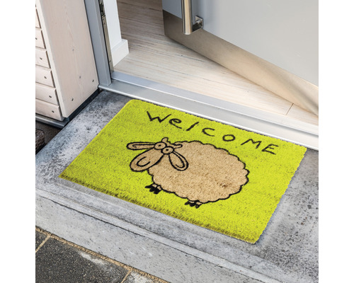 Fussmatte mit Willkommensaufschrift und Schafsmotiv vor einer geöffneten Tür