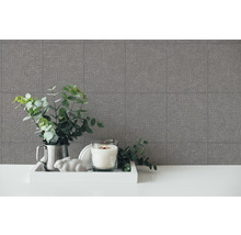 Dekoratives Arrangement mit gemusterter Tapete, Kerze und Grünpflanzen auf einem Tisch